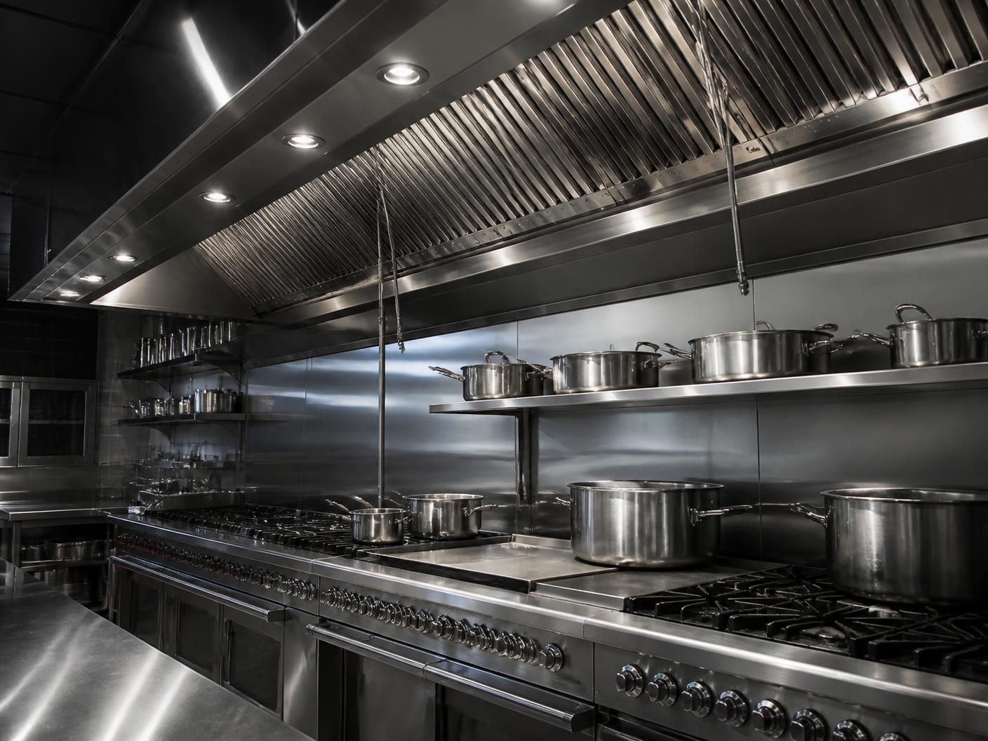 Commercial kitchen cooking line beneath a clean stainless steel exhaust hood